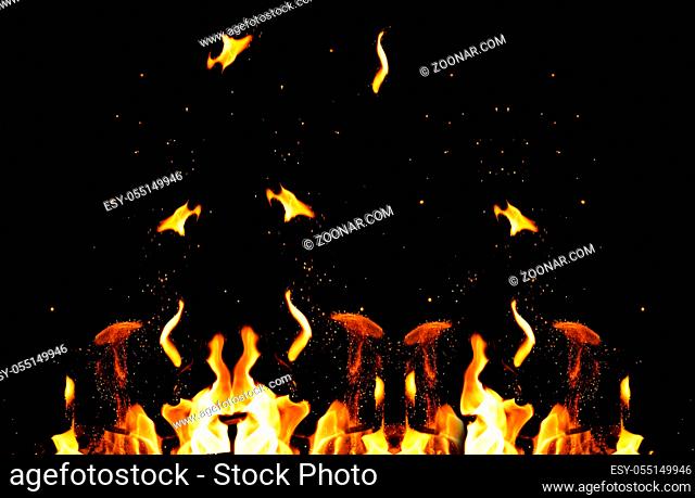 large burning bonfire with flame and orange sparks that fly in different directions on a black background, full frame