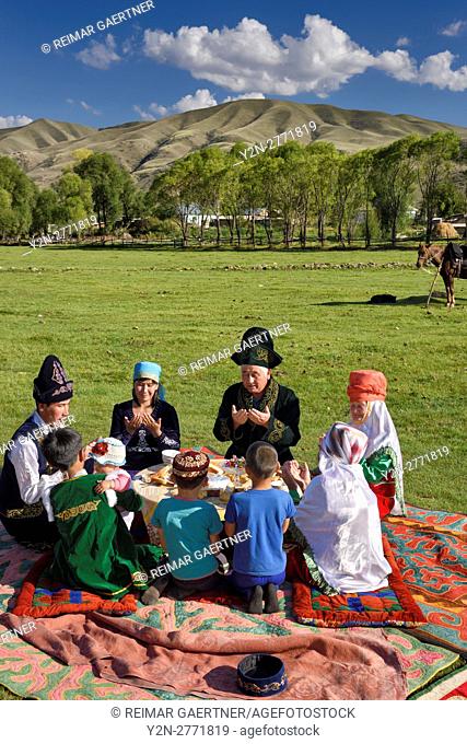 Kazakh family in traditional clothes praying before a picnic meal in pastureland at Saty Kazakhstan