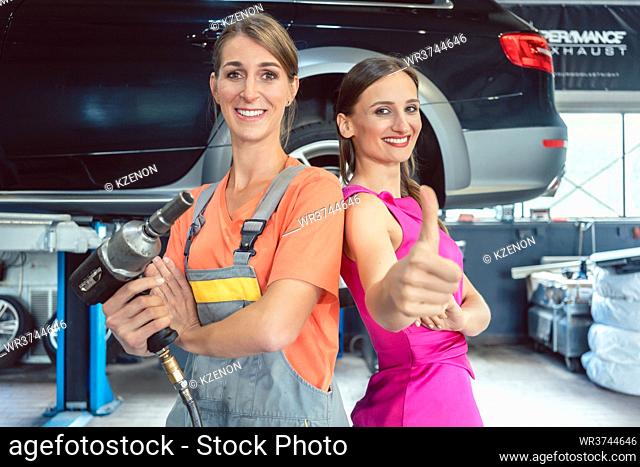 Portrait of a cheerful and beautiful female auto mechanic, looking at camera with confidence next to her happy customer in a cool modern automobile repair shop