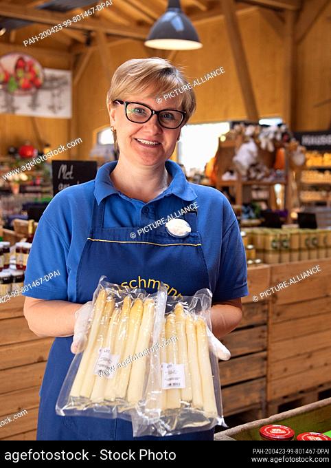 21 April 2020, Brandenburg, Beelitz/Gemeinde Klaistow: Saleswoman Iwona shows two packets of pre-cooked fresh asparagus in the farm shop