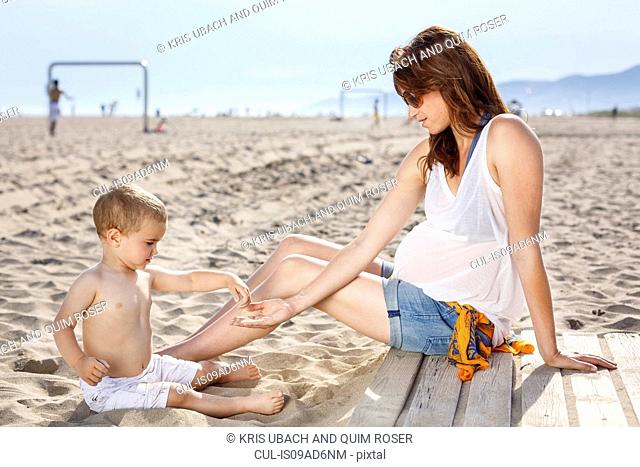 Baby on beach tipping sand onto mother's hand