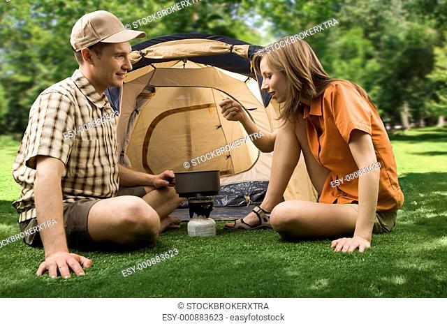 Photo of cheerful girl holding cup while her boyfriend pouring tea into it in the park
