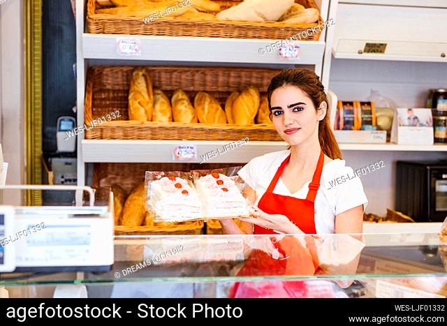 Young woman working in a bakery, showing cream cake