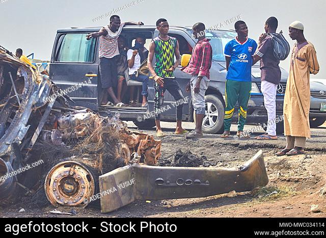 People passing by look at damaged vehicles at a site following an explosion after a tanker carrying fuel crashed at Kara Bridge along the Lagos-Ibadan highway