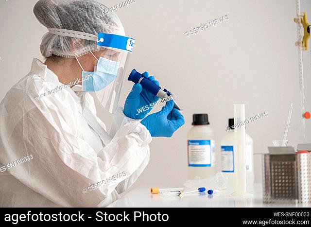 Woman in protective wear sitting at desk researching on epidemiology