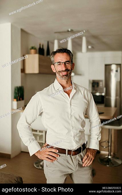 Smiling businessman with hands on hips in kitchen at home