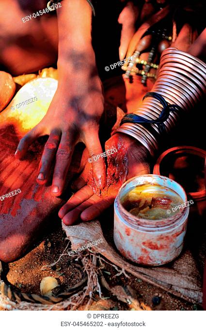 Himba woman mixing red ochre with petroleum jelly