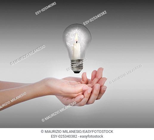 On hands levitates a broken bulb, inside there is a candle, with the flame lit, in front of a dark gray background