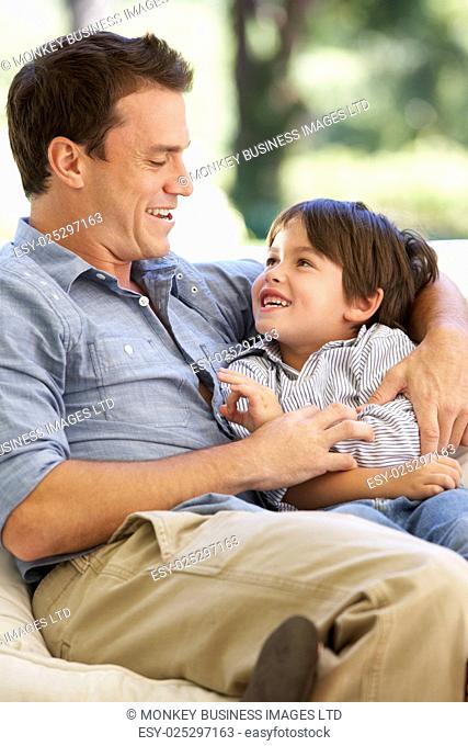 Father And Son Sitting On Sofa At Home