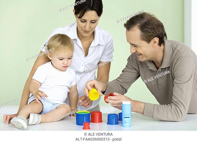 Father showing toddler plastic toys, mother watching