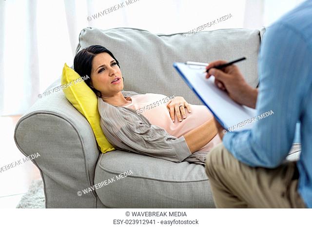 Doctor writing on clipboard while consulting pregnant woman