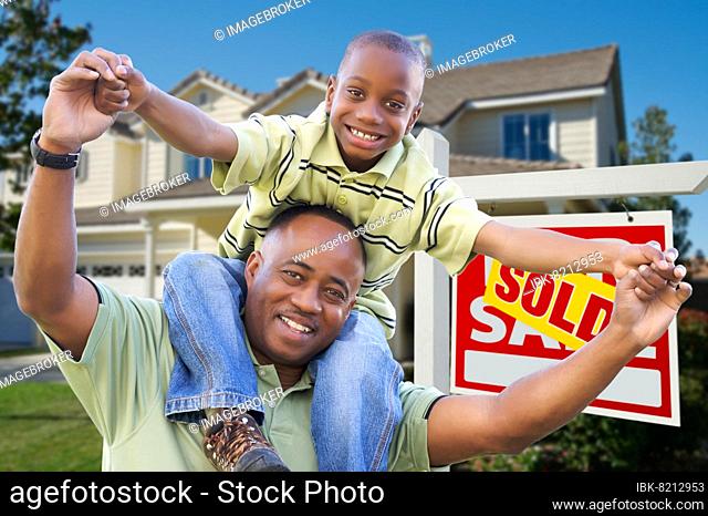 Happy african american father and son in front of new home and sold real estate sign