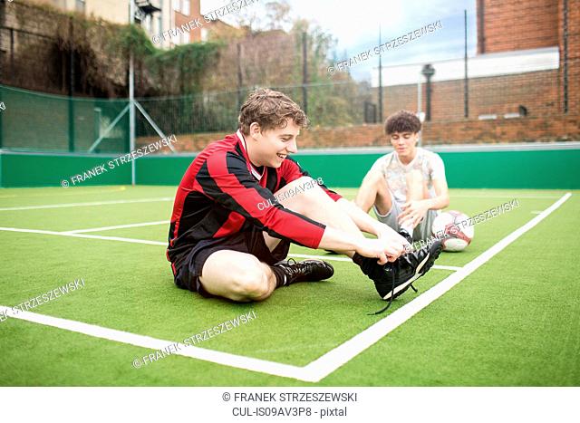 Two young men on urban football pitch, tying shoelaces
