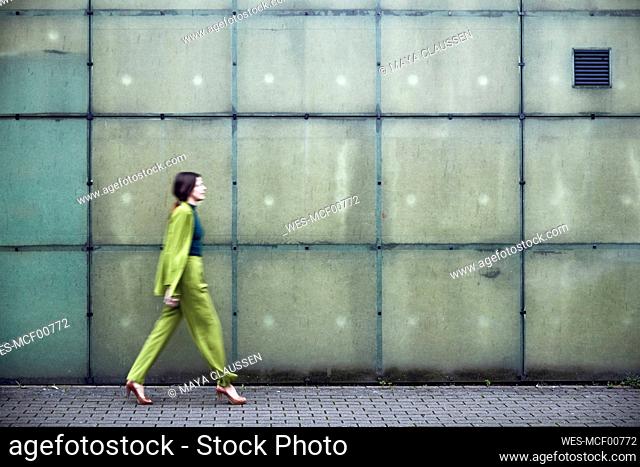 Businesswoman wearing green suit passing a wall