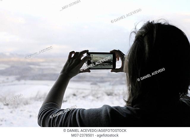 Woman taking winter landscape pictures with ther smartphone from her living room. Rioja wine region, Spain