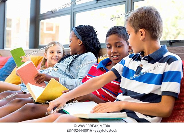 School kids sitting on sofa and reading book in library