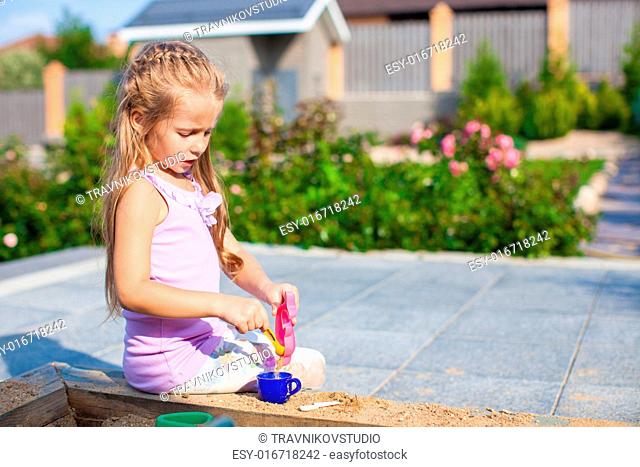 Little cute girl playing at the sandbox with toys in the yard