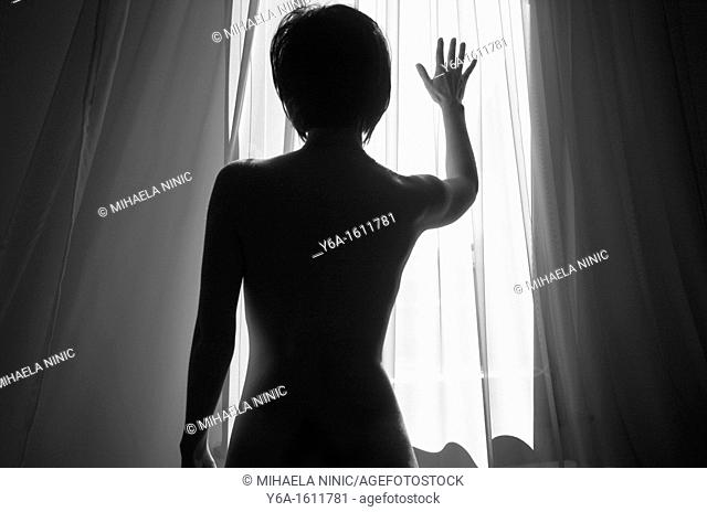 Woman silhouetted against window light placing hand on window