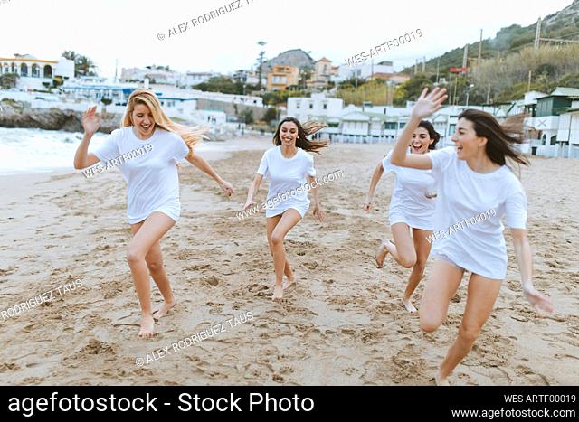 Young female friends running on sand while having fun during vacations