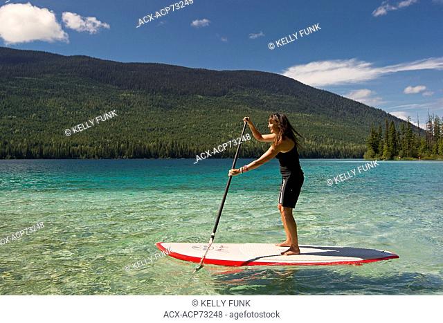 A female paddle boarder makes her way across the beautiful waters of Johnson Lake, North of Kamloops in the Thompson Okanagan region of British Columbia, Canada