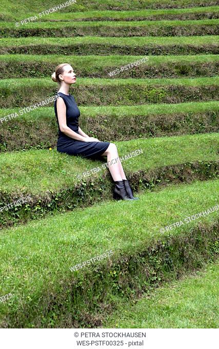 Italy, Alto Adige, Lana, woman sitting on grass-covered steps of natural open air theater