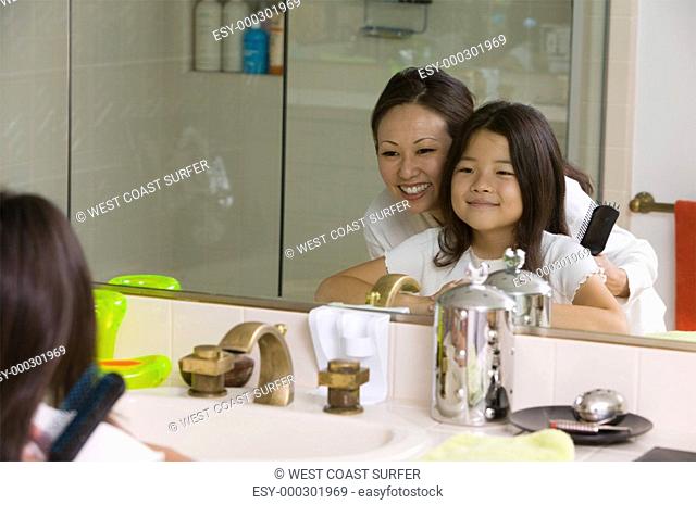 Mother and Daughter Looking at reflection in Bathroom mirror focus on mirror
