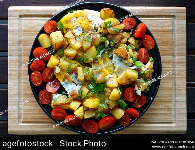 20 July 2021, Berlin: Fried potato pieces, halved mini tomatoes, the greens of spring onions and eggs are arranged on a plate after frying