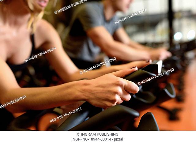 Two people biking in the gym, exercising legs doing cardio workout cycling bikes. Couple in a spinning class wearing sportswear