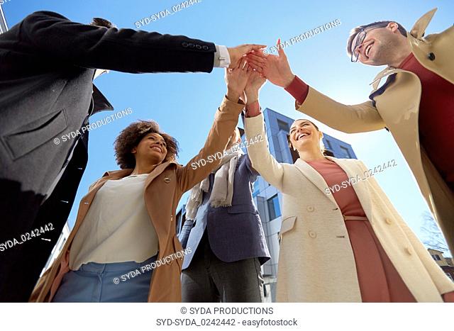 group of happy people making high five in city