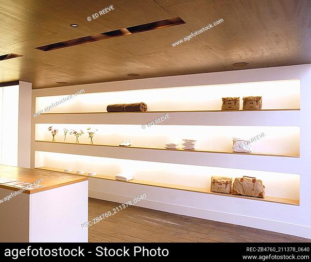 Interior of retail designer clothes shop fixed wooden shelves neatly placed white accessories bags towels Interiors shops shopping modern design pillows three...