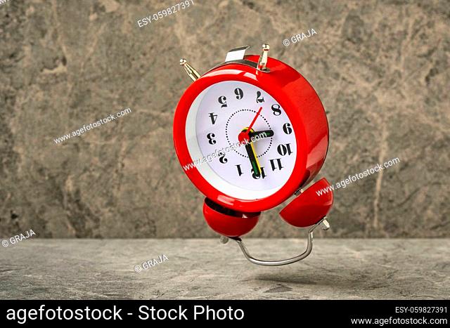 Red alarm clock falling on the stone background. Red alarm clock showing 9 o'clock in a morning