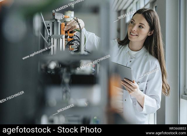 Smiling female scientist holding digital tablet inventing machinery in laboratory