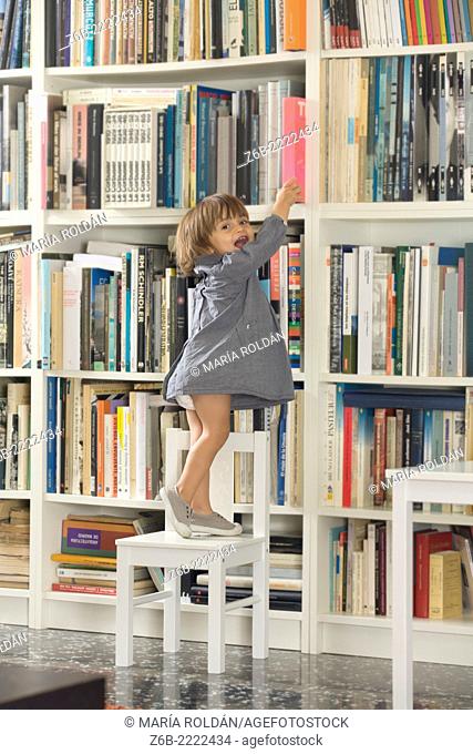 22 months old baby girl trying to reach a book from the bookshelves