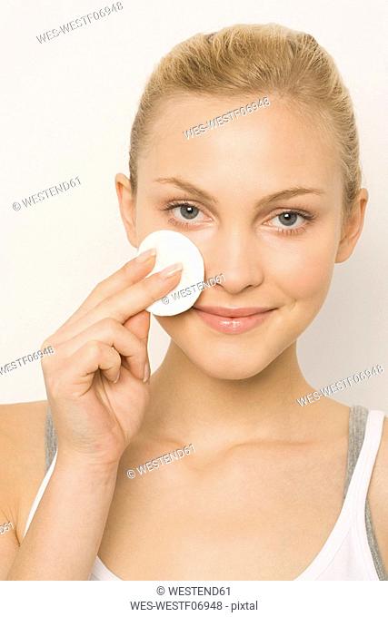 Young woman using cotton pad on face, portrait