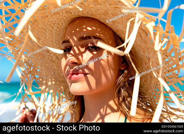 Side view of a Caucasian woman wearing a straw hat, sunbathing and smiling to camera. Weekend beach vacation, lifestyle and leisure