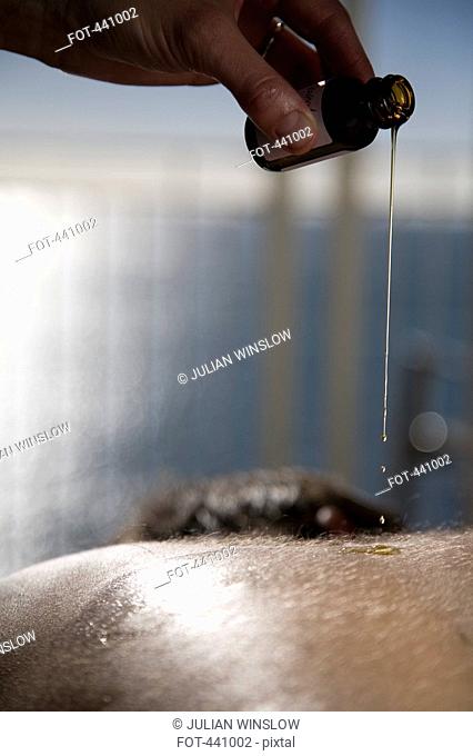 Close-up of a massage therapist pouring oil on a man's back
