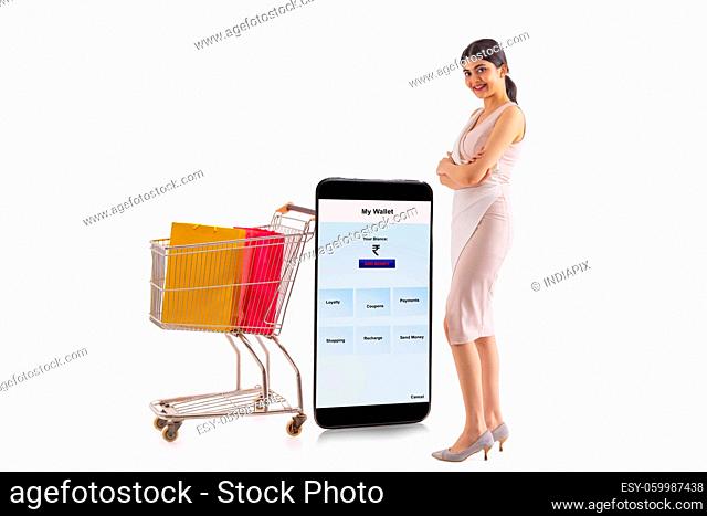 A young woman standing beside a mobile phone and cart of shopping bags