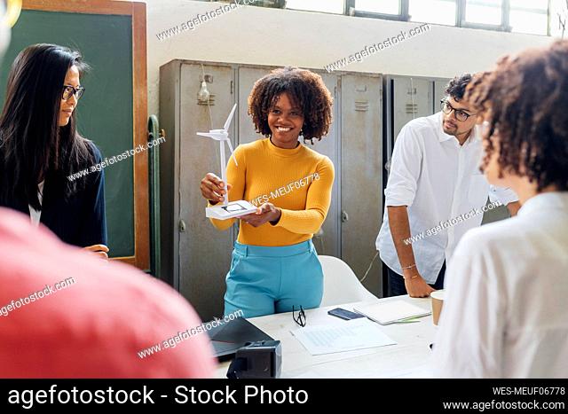 Smiling businesswoman showing wind turbine model to colleagues in office