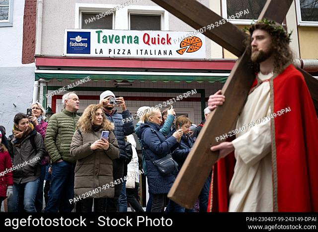 07 April 2023, Hesse, Bensheim: Jesus (Julian Lux) carries the cross through the city center past a pizzeria during the Good Friday procession