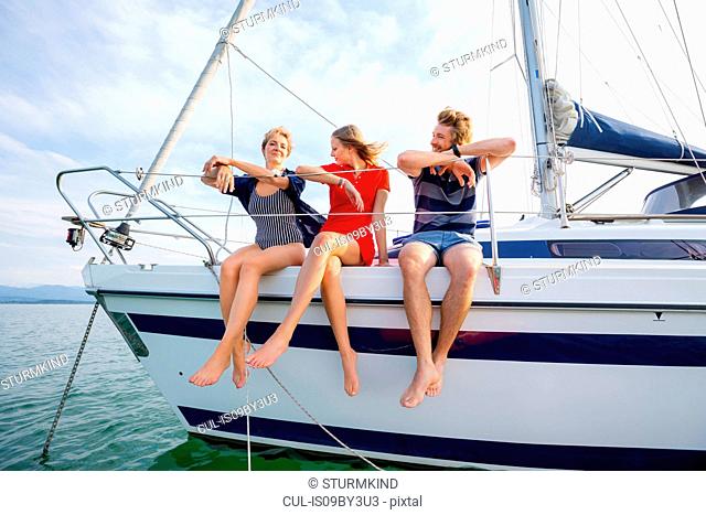 Mature woman and young adults sitting on sailboat on Chiemsee lake, Bavaria, Germany