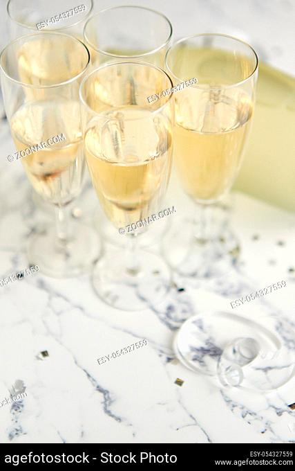 Champagne glasses and bottle placed on white marble background. Party and holiday celebration concept with confetti and serpentines. With copy space