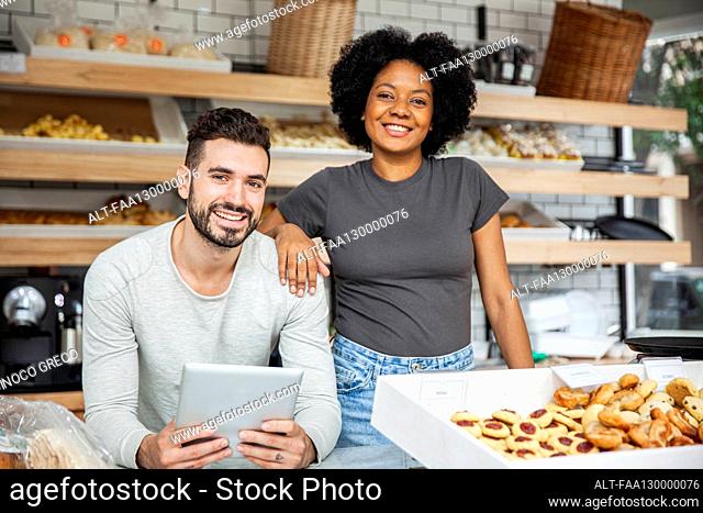 Bakery owners standing behind counter while holding digital tablet