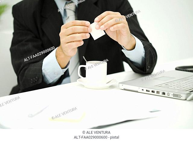 Man holding sugar packet over coffee cup, cropped view