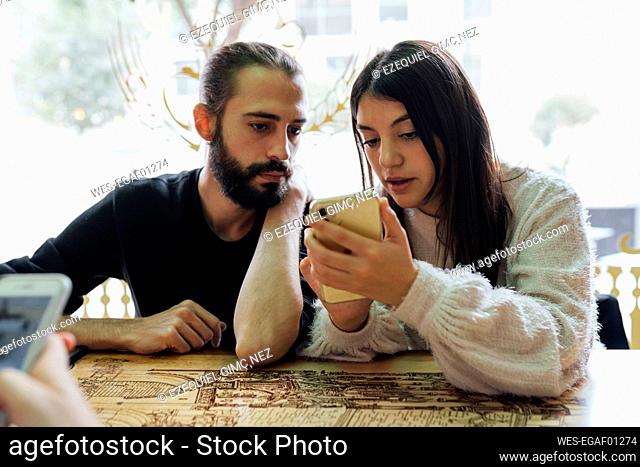 Young friends using smart phone while sitting in restaurant