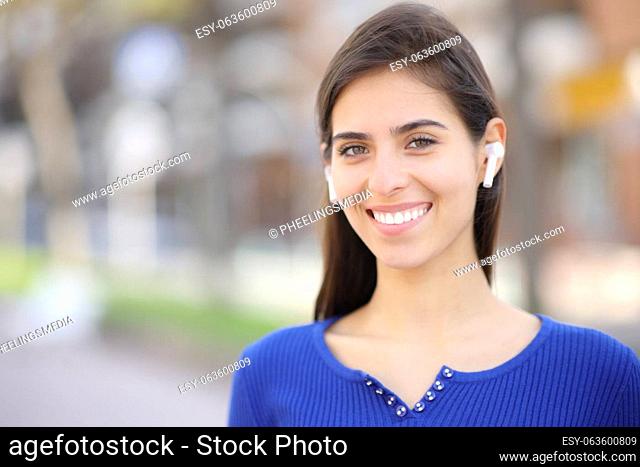 Happy woman with earphone standing and posing looking at camera in the street