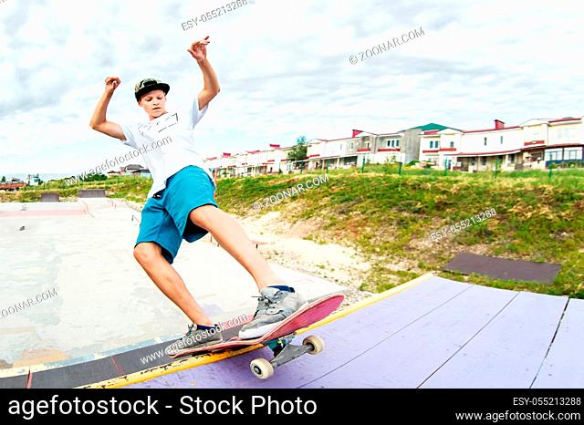 Teenager skater in a cap and shorts on rails on a skateboard in a skate park Wide angle
