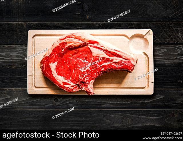 Raw beef prime rib on a cutting board. black wood background. Top view