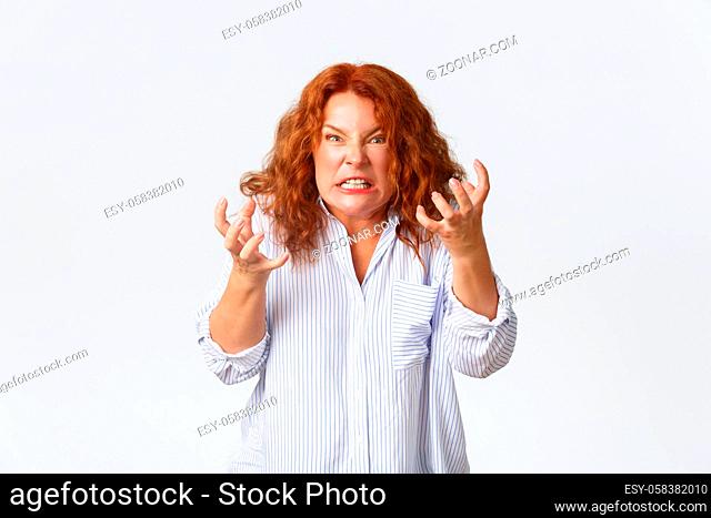 Angry and hateful middle-aged redhead woman looking outraged and bothered, grimacing from hatred, furiously clenching fists as want to kill someone