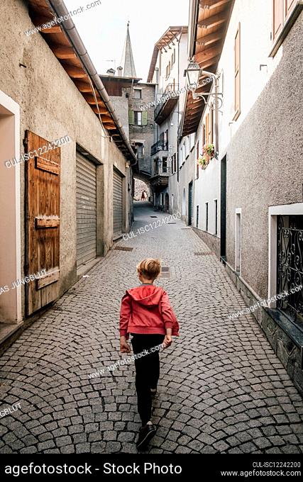 Rear view of boy walking down a narrow lane in Bormio, Lombardy, Italy