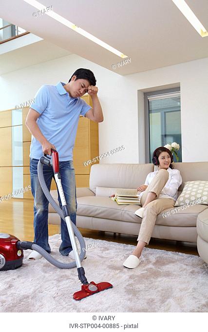 Woman On Couch Listening Music And Man Vacuuming